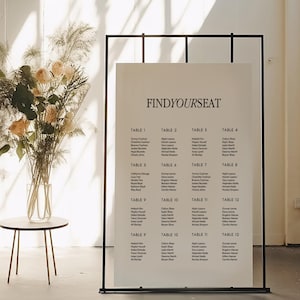 May include: A white poster with black text on a black easel stand. The poster says "FINDYOURSEAT" and lists names under each table number from 1 to 12.