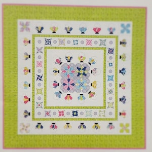 May include: A quilt block pattern with a central square surrounded by a ring of smaller squares. The pattern is made up of various colors and fabrics, including pink, blue, green, and white. The quilt block is framed by a green border with a pink outer border.