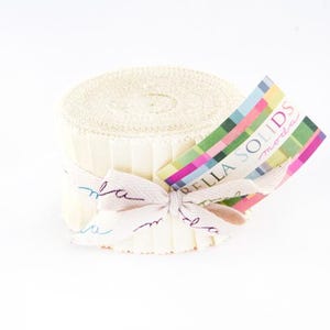 May include: A roll of cream-colored fabric strips tied with a cream ribbon and a tag. The ribbon is tied in a bow and has cursive writing. The tag has a colorful geometric design and the words "BELLA SOLIDS moda".