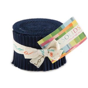 May include: A roll of navy blue fabric strips, tightly wound and secured with a cream-colored ribbon tied in a bow. A colorful tag with the text "MODA SOLIDS" is attached. The fabric is likely for quilting or crafting.