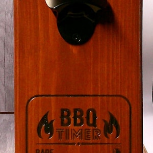 May include: A wooden BBQ timer and bottle opener combo. The wooden board is stained a reddish-brown color. The black bottle opener is mounted at the top. The timer has settings for rare, medium, and well done.