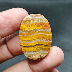 Pode incluir: Um cabochão de ágata amarelo, laranja e branco com uma forma oval lisa.
