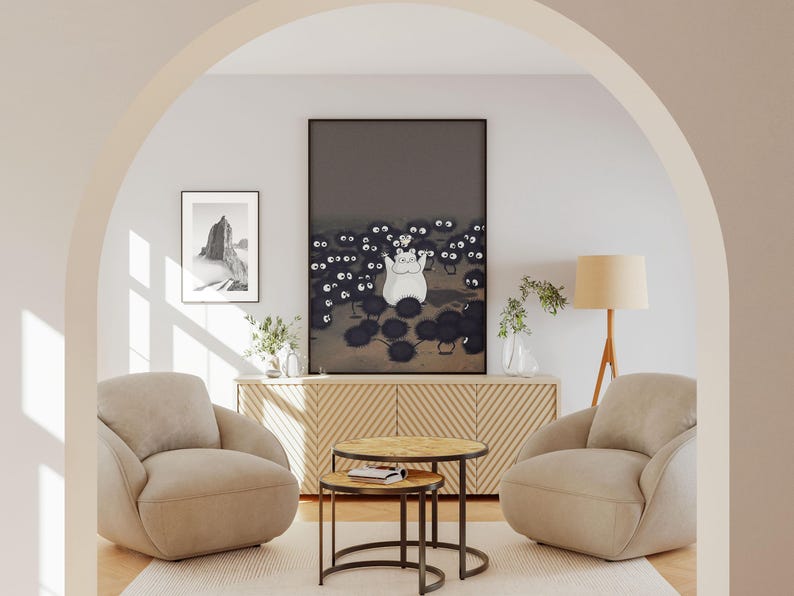 May include: A living room scene featuring two beige armchairs, a wooden cabinet, and two round coffee tables. A large framed print depicts a white cartoon character surrounded by black soot sprites. A smaller framed print shows a black and white landscape.