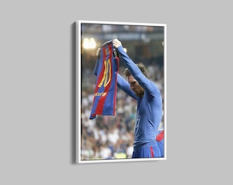May include: A soccer player in a blue jersey holds up a blue and red jersey with the number 10 on it. The player is surrounded by a crowd of people.