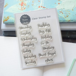 Set of clear stamps with calligraphy days of the week and other planner words like birthday and day off. The stamp set is leaning against a stack of notebooks.