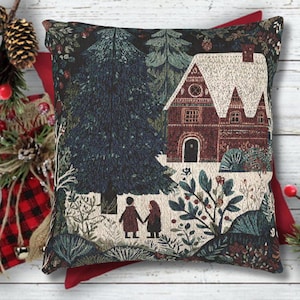May include: Decorative square pillow with a tapestry design featuring a winter scene. The pillow depicts a house with a snow-covered roof, surrounded by trees and foliage. Two figures are holding hands in the foreground. The color palette includes shades of green, brown, and white.
