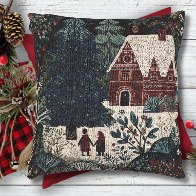 May include: Decorative square pillow with a tapestry design featuring a winter scene. The pillow depicts a house with a snow-covered roof, surrounded by trees and foliage. Two figures are holding hands in the foreground. The color palette includes shades of green, brown, and white.