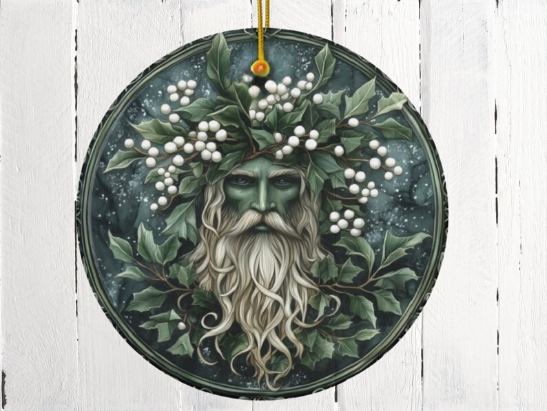 May include: A round, green and white Christmas ornament featuring a stylized image of the Green Man, a mythical figure associated with nature and the changing seasons. He is depicted with a beard and hair made of leaves and berries, and his face is framed by a wreath of holly.