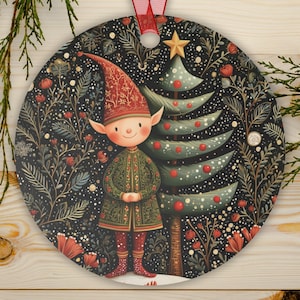 May include: A round Christmas ornament featuring a whimsical elf standing next to a decorated Christmas tree. The elf wears a red hat and green coat. The background is a dark floral pattern with a red ribbon for hanging.