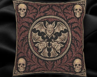 May include: Square black decorative pillow with a gothic design. The pillow features a central circular emblem with a bat and three smaller bats. The corners have skulls, and the border has a red and gold floral pattern.
