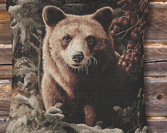 May include: A decorative pillow featuring a detailed tapestry design of a brown bear in a forest setting. The bear is the focal point, surrounded by foliage and berries, with a rustic, natural aesthetic.