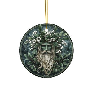 May include: A round ceramic ornament featuring a green-skinned man with a long white beard and a crown of white berries and green leaves. The background is a dark blue with white speckles.