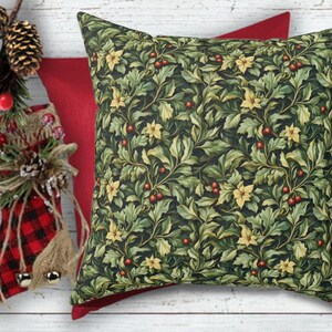May include: A decorative square pillow with a dark green background and a pattern of green leaves, yellow flowers, and red berries. A solid red pillow is behind it. The pillow is part of a holiday or seasonal collection.