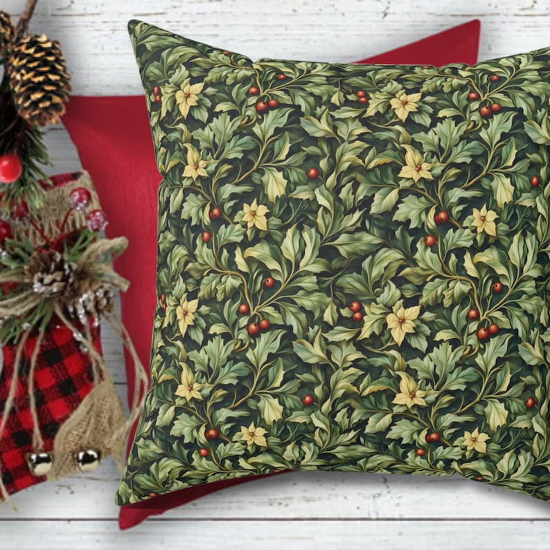May include: A decorative square pillow with a dark green background and a pattern of green leaves, yellow flowers, and red berries. A solid red pillow is behind it. The pillow is part of a holiday or seasonal collection.