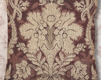 May include: Square decorative pillow with a detailed damask pattern in shades of brown and beige. The pillow features a symmetrical floral design, creating a classic and elegant look. The fabric has a textured appearance.