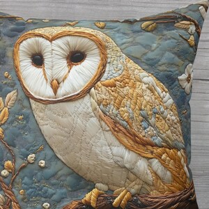 May include: Decorative pillow featuring an embroidered owl design. The owl has a white face, brown eyes, and tan and brown feathers. The background is a textured blue fabric with floral accents. The pillow is square.