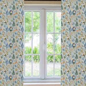 Puede incluir: Un par de cortinas azules con un patr&oacute;n repetitivo de personas sentadas en un bosque con &aacute;rboles, flores y p&aacute;jaros. Las cortinas est&aacute;n colgadas frente a una ventana con vista a un follaje verde.