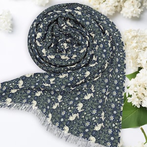 May include: A blue scarf with a white rabbit and floral pattern. The scarf has a fringed edge.