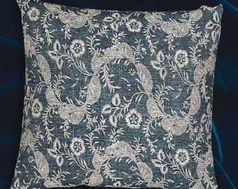 May include: Square decorative pillow with a dark blue background and a repeating pattern of white floral and leaf designs. The pillow has a textured appearance and is likely made of fabric.