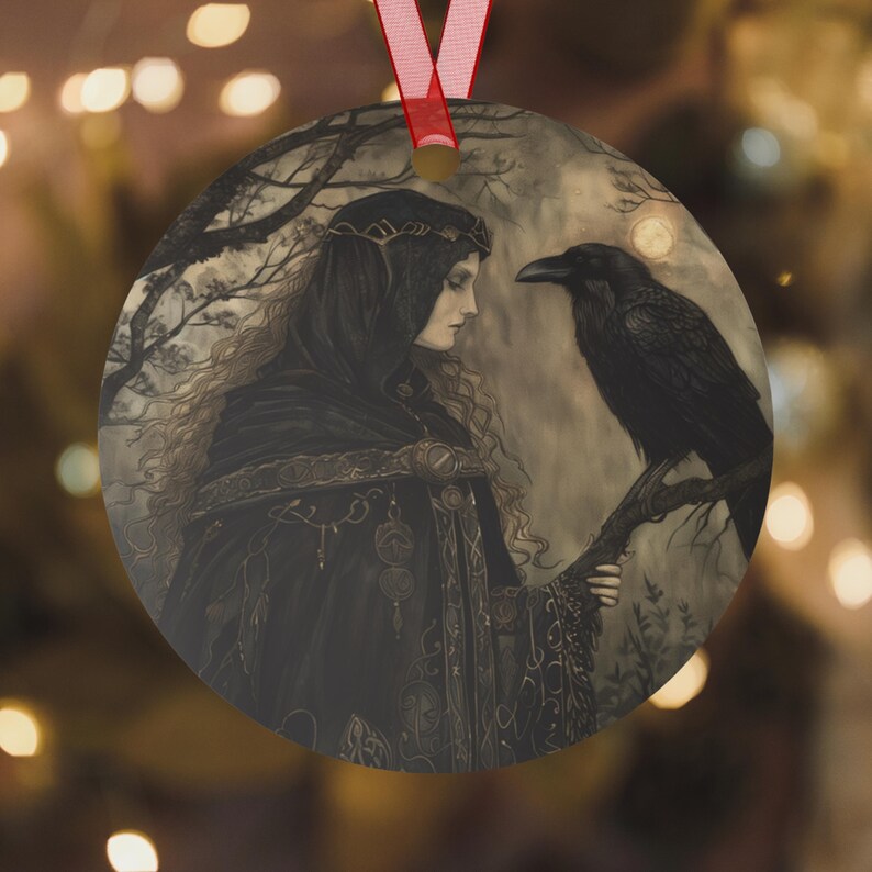 May include: Round Christmas ornament featuring a gothic illustration of a woman in a black hooded cloak with a raven perched on a branch. The artwork has a mystical, fantasy theme with a red ribbon for hanging.