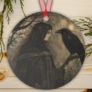Metal ornament depicting the Celtic goddess The Morrigan in dark robes with a raven on her arm beneath a glowing moon.