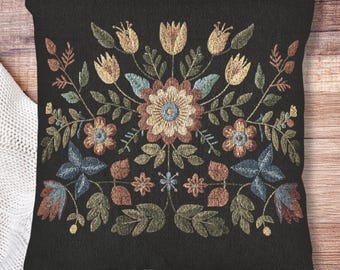 May include: Black square throw pillow with an embroidered floral design. The design features a central flower with surrounding flowers, leaves, and stems in shades of yellow, blue, brown, and green.
