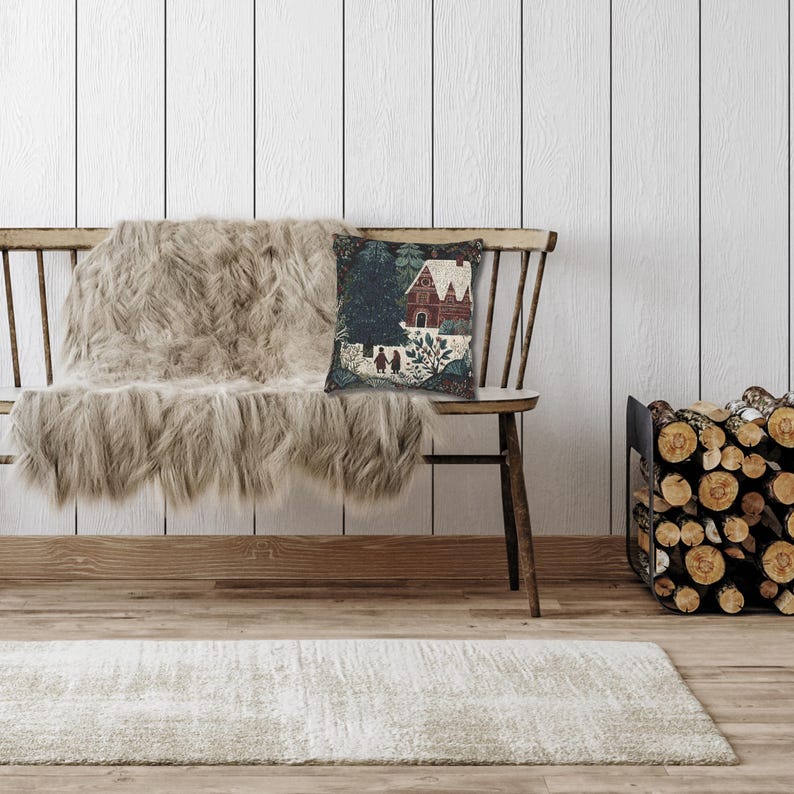 May include: A cozy interior scene featuring a wooden bench with a faux fur throw and a decorative pillow. The pillow displays a quaint house scene. A stack of firewood sits nearby, and a rug lies on the floor. The walls are white with vertical wood paneling.
