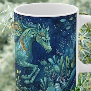 May include: White ceramic mug featuring a detailed illustration of a teal and gold horse against a dark blue background. The horse design is surrounded by stylized plants and foliage, creating a whimsical and artistic aesthetic.