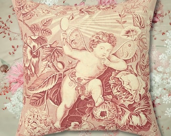 May include: A pink throw pillow with a vintage illustration of a cherub with wings holding a mirror, surrounded by floral designs.