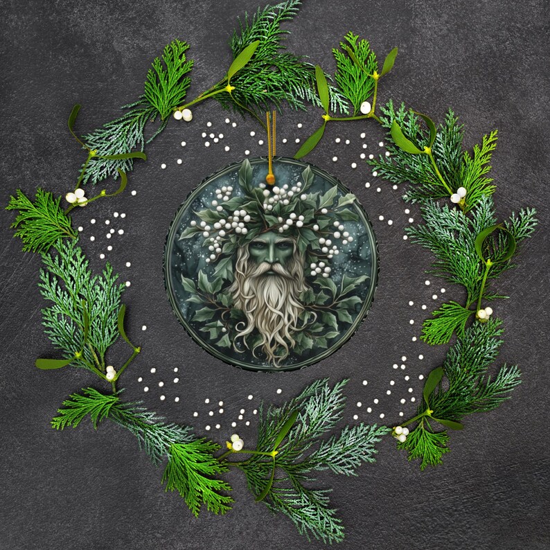 May include: A round, green and white Christmas ornament featuring a green man with a long white beard and a crown of leaves and white berries. The ornament is surrounded by a wreath of green leaves and white berries.