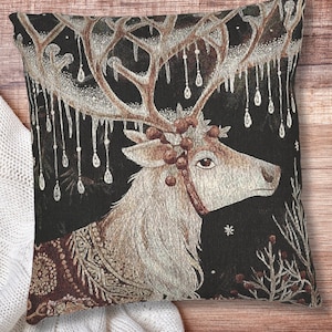 May include: Decorative square pillow featuring a detailed illustration of a reindeer with large antlers adorned with icicles and berries. The reindeer has a detailed coat and is set against a dark background with wintery accents. The pillow has a brown and black color scheme.