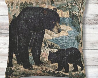 May include: A square throw pillow featuring a woven tapestry design of a large black bear standing beside a smaller black bear cub. The scene depicts a forest landscape with trees, foliage, and a blue stream in the background, rendered in shades of black, brown, tan, and muted blue.