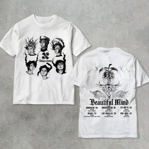 May include: White t-shirts with black graphic designs. One shirt features portraits and the text "Xdinary Heroes." The other shirt displays an abstract design and the words "Beautiful Mind" with tour locations.