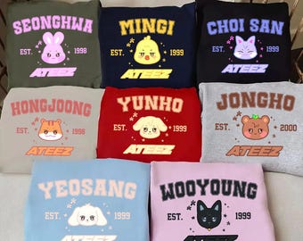 Puede incluir: Nueve sudaderas de diferentes colores con un animal de dibujos animados y el texto "ATEEZ" en cada una. Las sudaderas son todas de estilo universitario con el texto "EST." y un año.