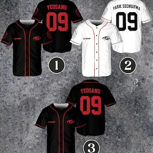 Peut inclure: Maillots de baseball noirs et blancs avec des détails rouges. Les maillots présentent les noms et numéros de joueurs, dont "Yeosang 09" et "Park Seonghwa 09". Chaque maillot a une fermeture boutonnée et des manches courtes. Les maillots ont le logo "ATEEZ".