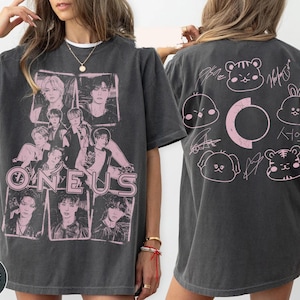 May include: A charcoal gray short-sleeve t-shirt featuring a pink graphic print. The front displays a collage of six individuals with the text ONEUS. The back shows a circular design with five cartoon animal faces and signatures.