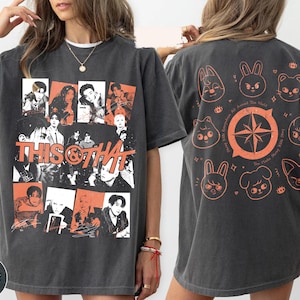 May include: A charcoal gray t-shirt featuring a front graphic collage of black and white portraits with orange accents and the text THIS & THAT. The back displays an orange compass design surrounded by eight stylized animal character illustrations.