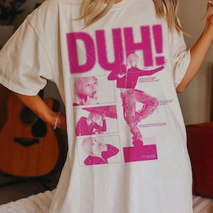 以下が含まれることがあります： アイボリー色のTシャツ。大きなピンク色のグラフィックで「DUH！」と書かれており、画像のコラージュが特徴です。グラフィックには、ピンクのパンツと黒いジャケットを着た人が含まれています。「IVORY」の文字が下部に印刷されています。