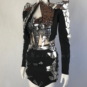 May include: A black dress and jacket set with silver mirrored detailing. The jacket has structured shoulders and a high collar. The dress features a matching mirrored design on the bodice and skirt. The outfit is displayed on a mannequin.