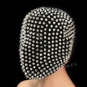 May include: A black mask densely covered in silver spikes. The spikes are uniformly distributed across the mask's surface, giving it a textured and bold look. The mask is designed to cover the whole face.