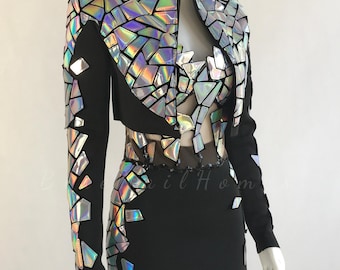 Puede incluir: Conjunto de vestido y chaqueta negros con detalles geométricos iridiscentes. La chaqueta tiene hombros estructurados y mangas largas. El vestido presenta un panel transparente en la cintura. Las formas geométricas reflejan un arcoíris de colores.