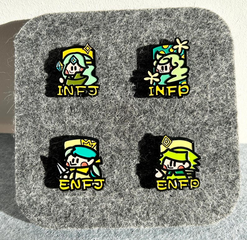 May include: Four enamel pins with cartoon characters and personality type acronyms. Each pin features a different character in shades of green, yellow, and blue, with the acronyms INFJ and ENFJ in yellow. The pins are displayed on a gray felt surface.