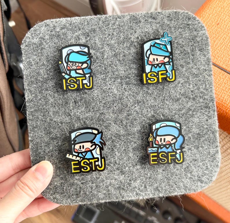 May include: Four personality type pins on a gray felt square. Each pin features a cartoon character in blue and white with a corresponding personality type abbreviation in yellow: ISTJ, ISFJ, ESTJ, and ESFJ.