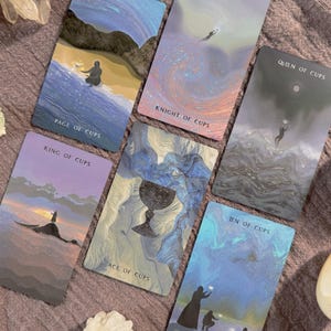 Może przedstawiać: Sześć kart tarota z akwarelowymi ilustracjami i tytułami takimi jak "Page of Cups", "Knight of Cups" i "Queen of Cups". Karty przedstawiają obrazy postaci, krajobraz&oacute;w i kielicha, z miękką, eteryczną paletą kolor&oacute;w.