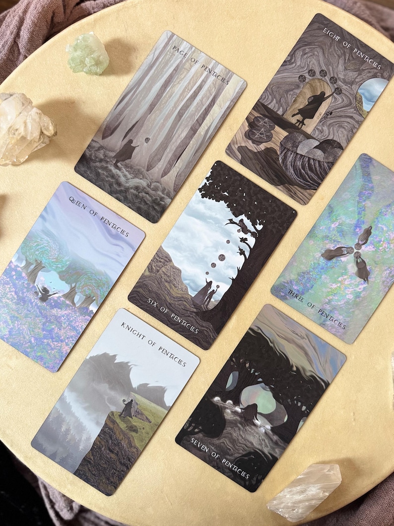 Może przedstawiać: Zestaw kart tarota z ilustracjami o tematyce przyrodniczej i fantasy. Karty wyświetlają tytuły takie jak "Page of Pentacles", "Queen of Pentacles" i "Eight of Pentacles". Karty są ułożone na jasnobrązowej powierzchni.