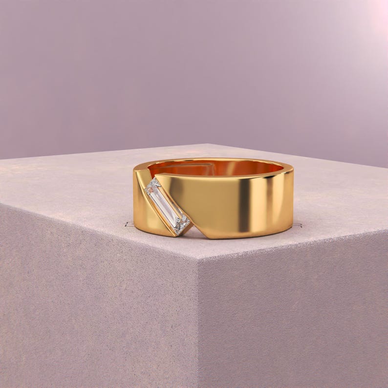 K&ouml;nnte beinhalten: Ein goldener Ring mit einem rechteckigen, klaren Edelstein, der diagonal &uuml;ber einem ausgeschnittenen Bereich eingesetzt ist. Der Ring ist dick und poliert und liegt auf einer hellgrauen Oberfl&auml;che vor einem weichen lila Hintergrund.
