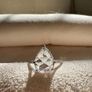 Front view of a pear shaped lab grown diamond engagement ring resting on a neutral jewelry cushion, displaying the brilliant pear cut center stone with a shimmering halo and pavé white gold band. The balanced proportions and exceptional sparkle highlight luxury craftsmanship and ethical sourcing. Perfect for buyers searching pear lab diamond engagement rings, eco friendly bridal jewelry, luxury diamond solitaires, and modern engagement ring styles.