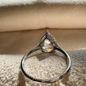 Rear profile view of a pear cut lab grown diamond ring placed on a soft jewelry cushion, highlighting the detailed halo setting and graceful band curvature. The elevated center stone enhances sparkle while the pavé white gold band adds subtle brilliance. This luxury engagement ring is ideal for buyers seeking pear shaped lab diamond rings, ethical engagement jewelry, modern bridal rings, sustainable fine jewelry, and handcrafted designer diamond rings.