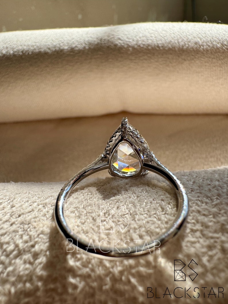 Rear profile view of a pear cut lab grown diamond ring placed on a soft jewelry cushion, highlighting the detailed halo setting and graceful band curvature. The elevated center stone enhances sparkle while the pavé white gold band adds subtle brilliance. This luxury engagement ring is ideal for buyers seeking pear shaped lab diamond rings, ethical engagement jewelry, modern bridal rings, sustainable fine jewelry, and handcrafted designer diamond rings.