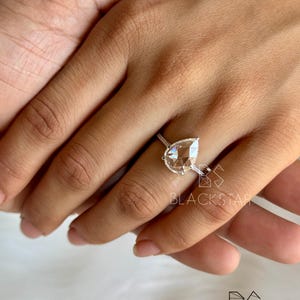 On-hand view of a luxurious pear shaped lab grown diamond engagement ring worn on finger, showcasing a brilliant pear cut center diamond with a delicate halo and pavé diamond band. Crafted in polished white gold, this elegant ring highlights exceptional sparkle, balanced proportions, and refined craftsmanship. Ideal for buyers searching pear diamond engagement rings, lab created diamond jewelry, ethical bridal rings, modern luxury engagement rings, and sustainable fine jewelry.